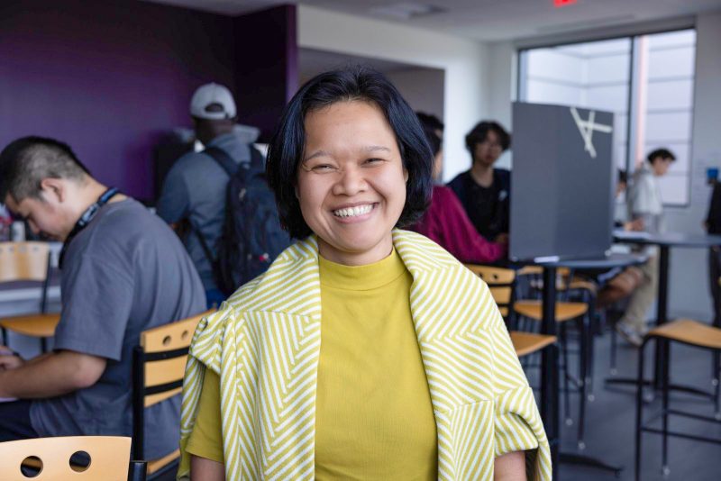 Maria Prawati smiles at the camera with students working behind her